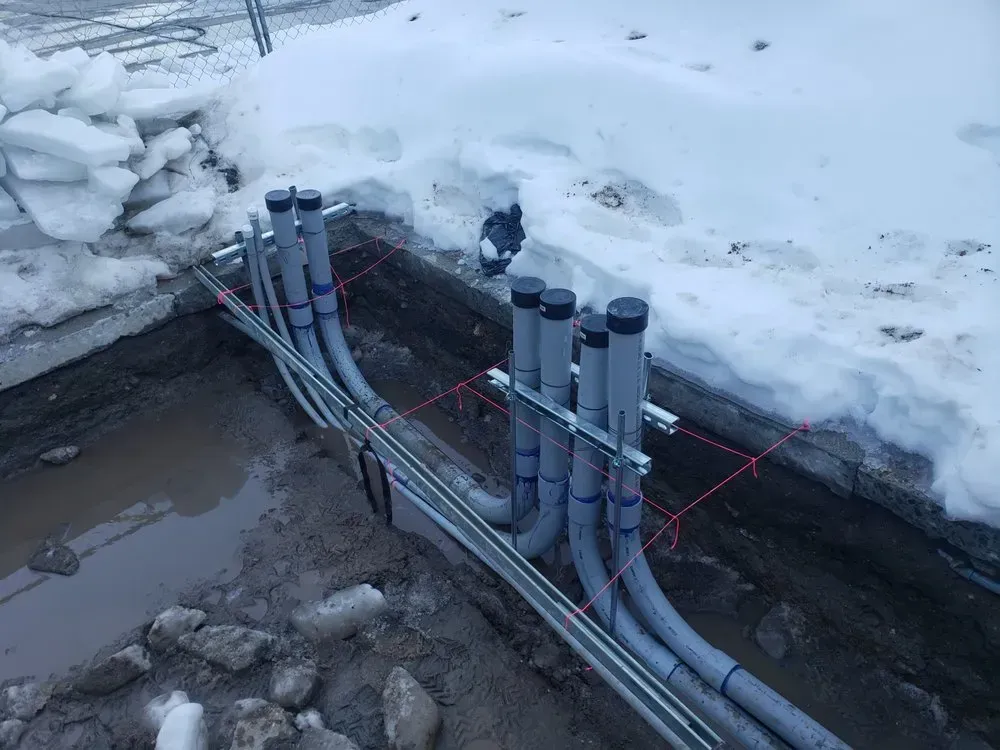 A bunch of pipes are laying in the dirt in the snow.