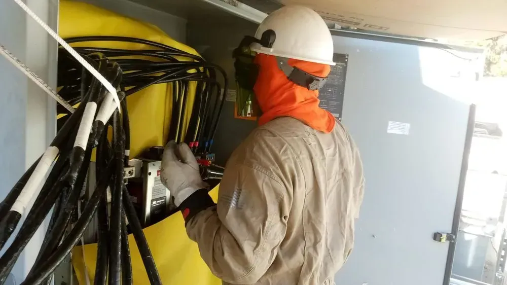A man in a hard hat is working on a electrical box.