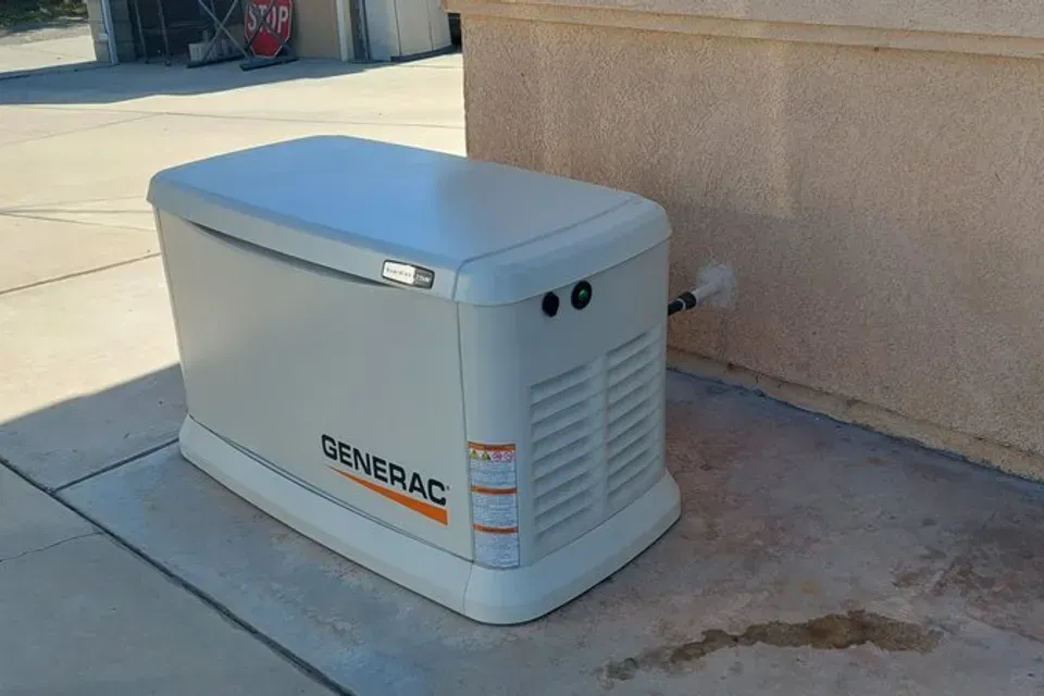 A generator is sitting on the sidewalk next to a wall.