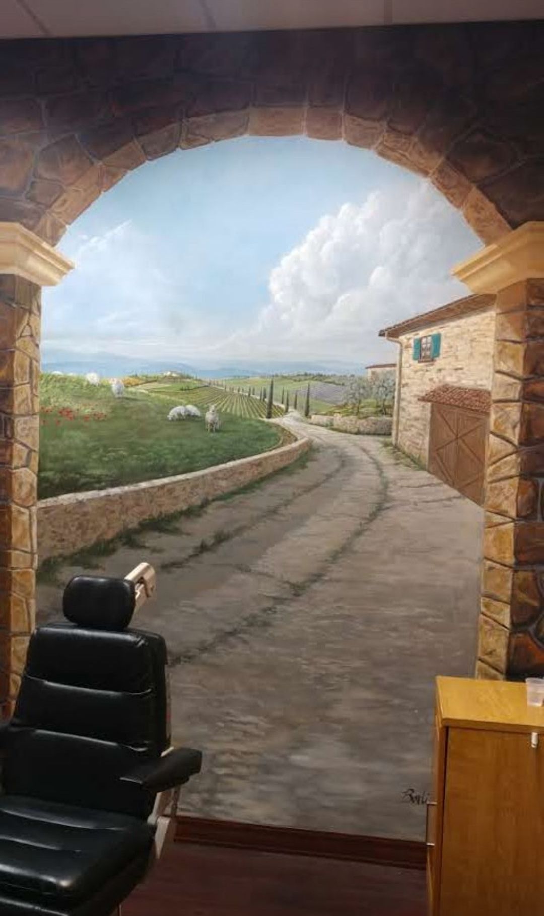 A chair is sitting in front of a painting of a country road.