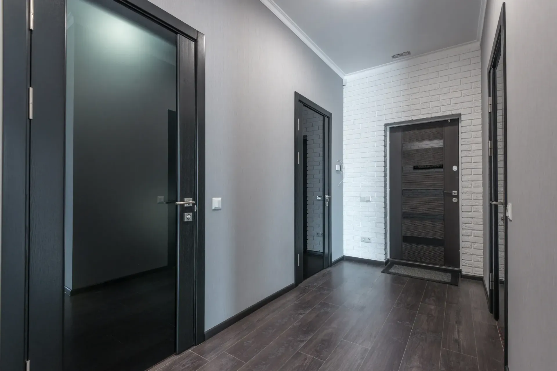 A hallway with black doors and a brick wall.