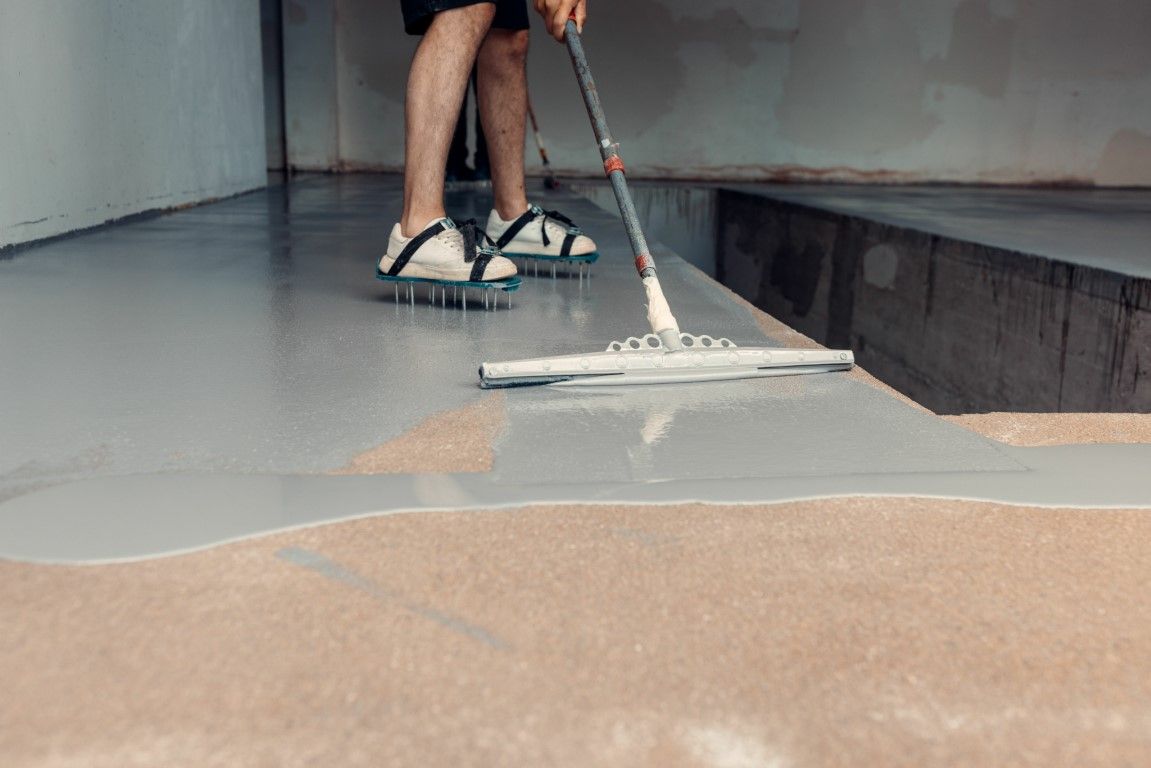 Person applying epoxy coating to a floor with a squeegee in a basement.