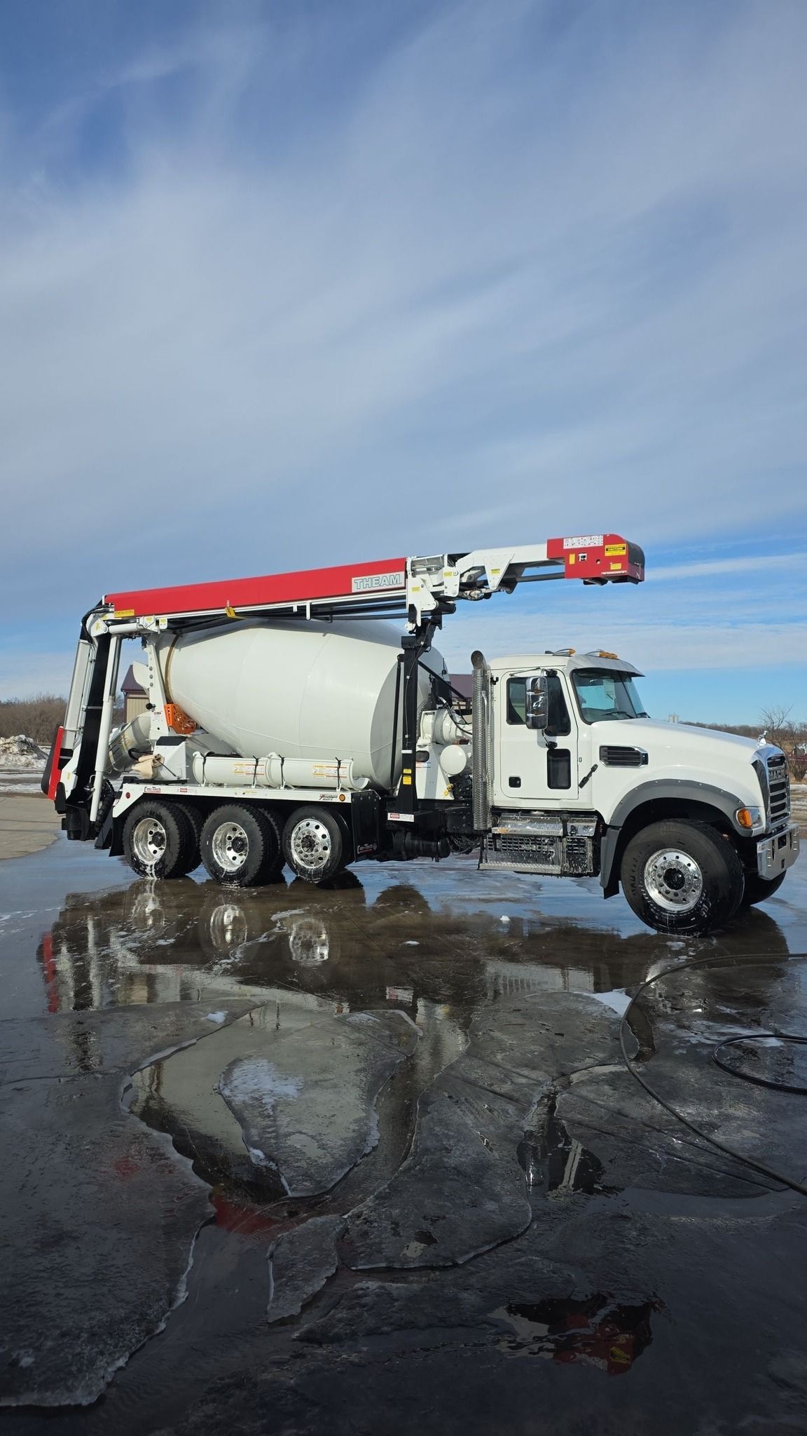 White utility truck with red boom arm on a wet road beside standing water under a cloudy sky