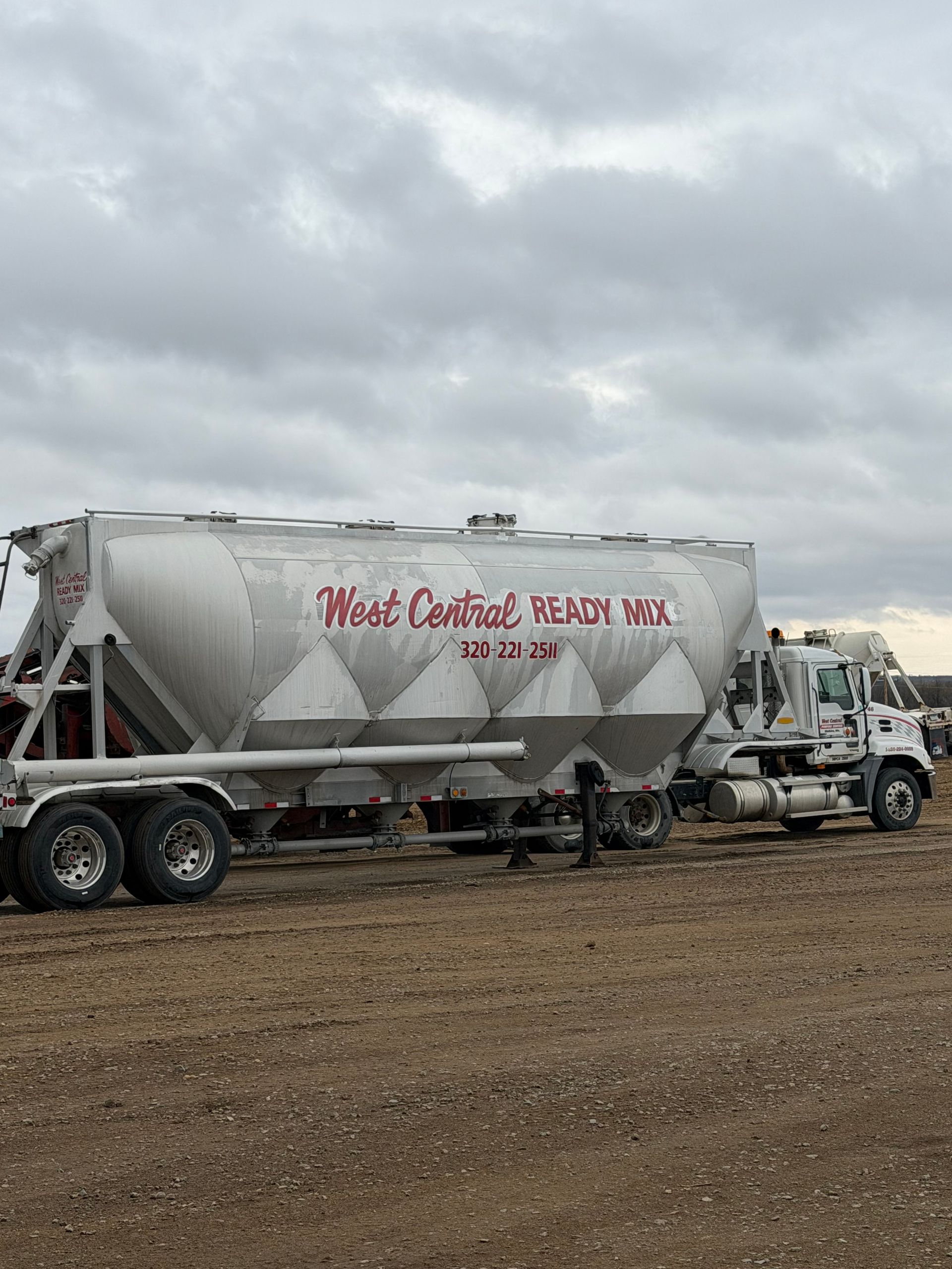White cement mixer truck parked on a gravel lot under a cloudy sky