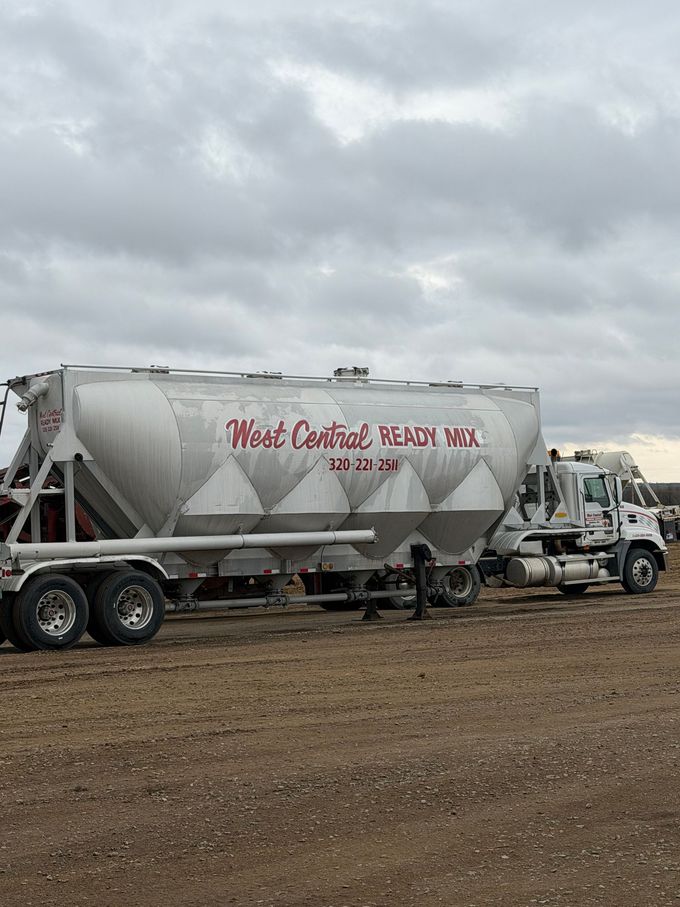 White cement tanker truck on a gravel lot under cloudy skies