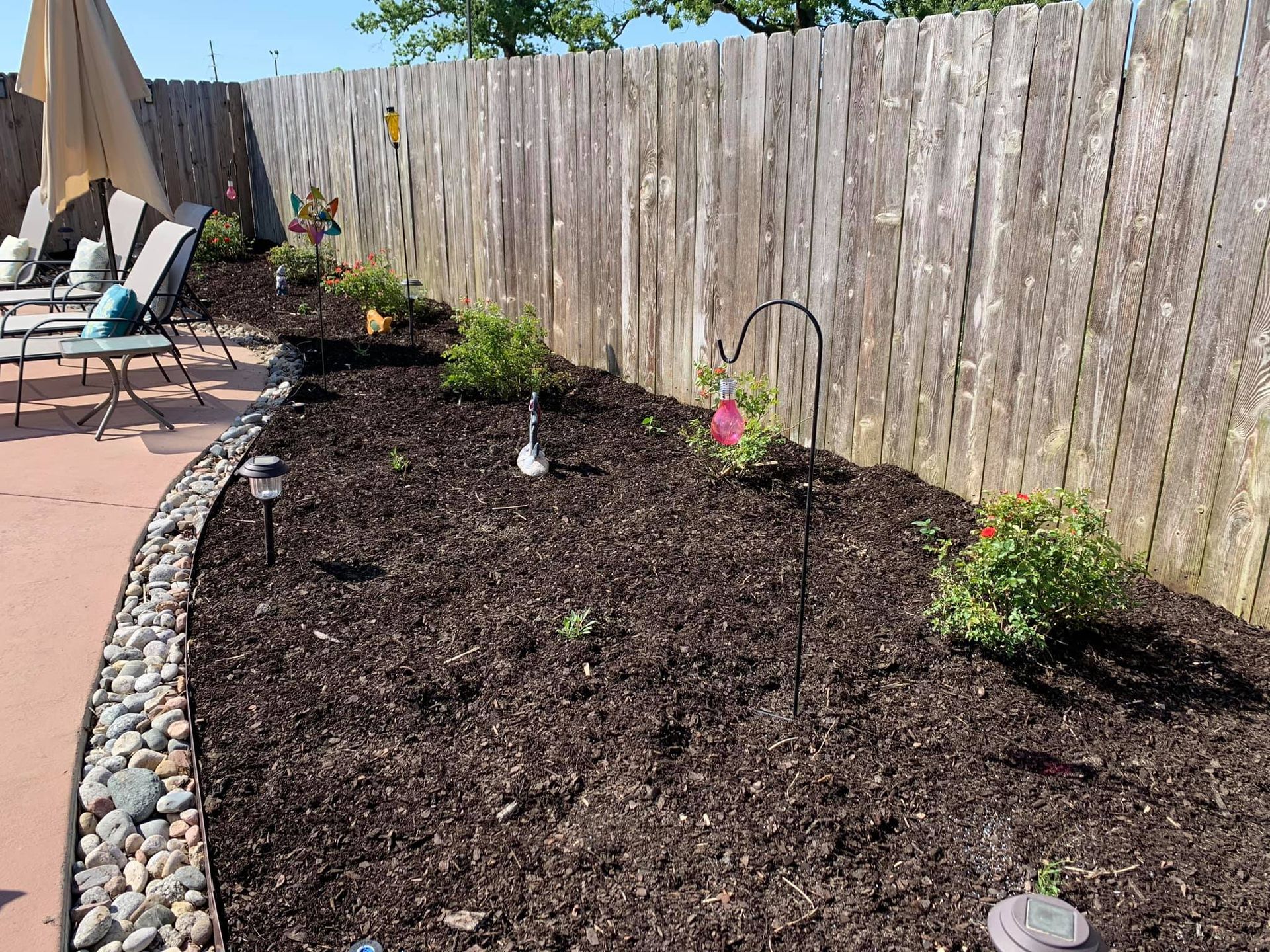 A garden with a wooden fence and a patio in the background.