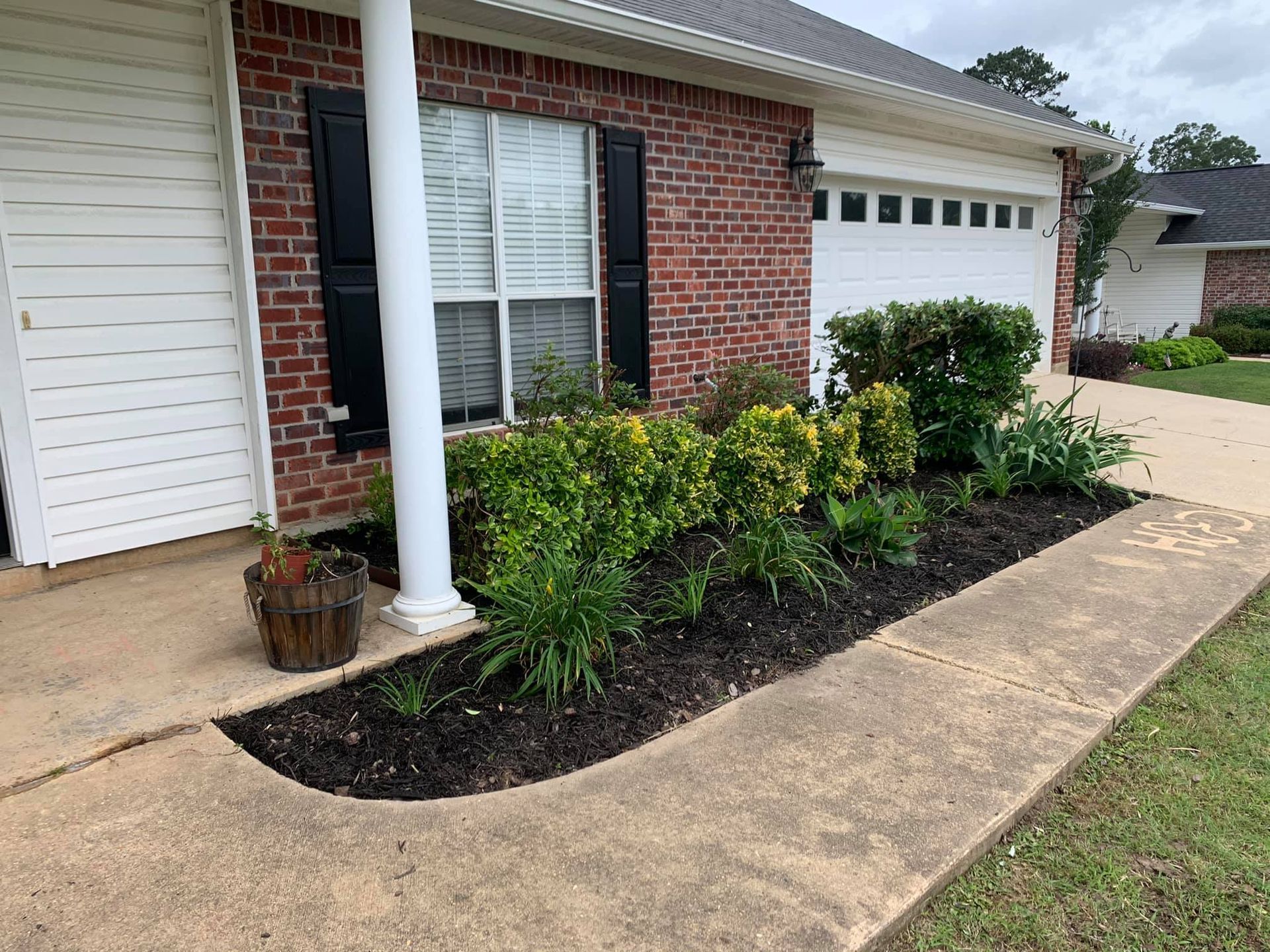 A brick house with a white garage door and a garden in front of it
