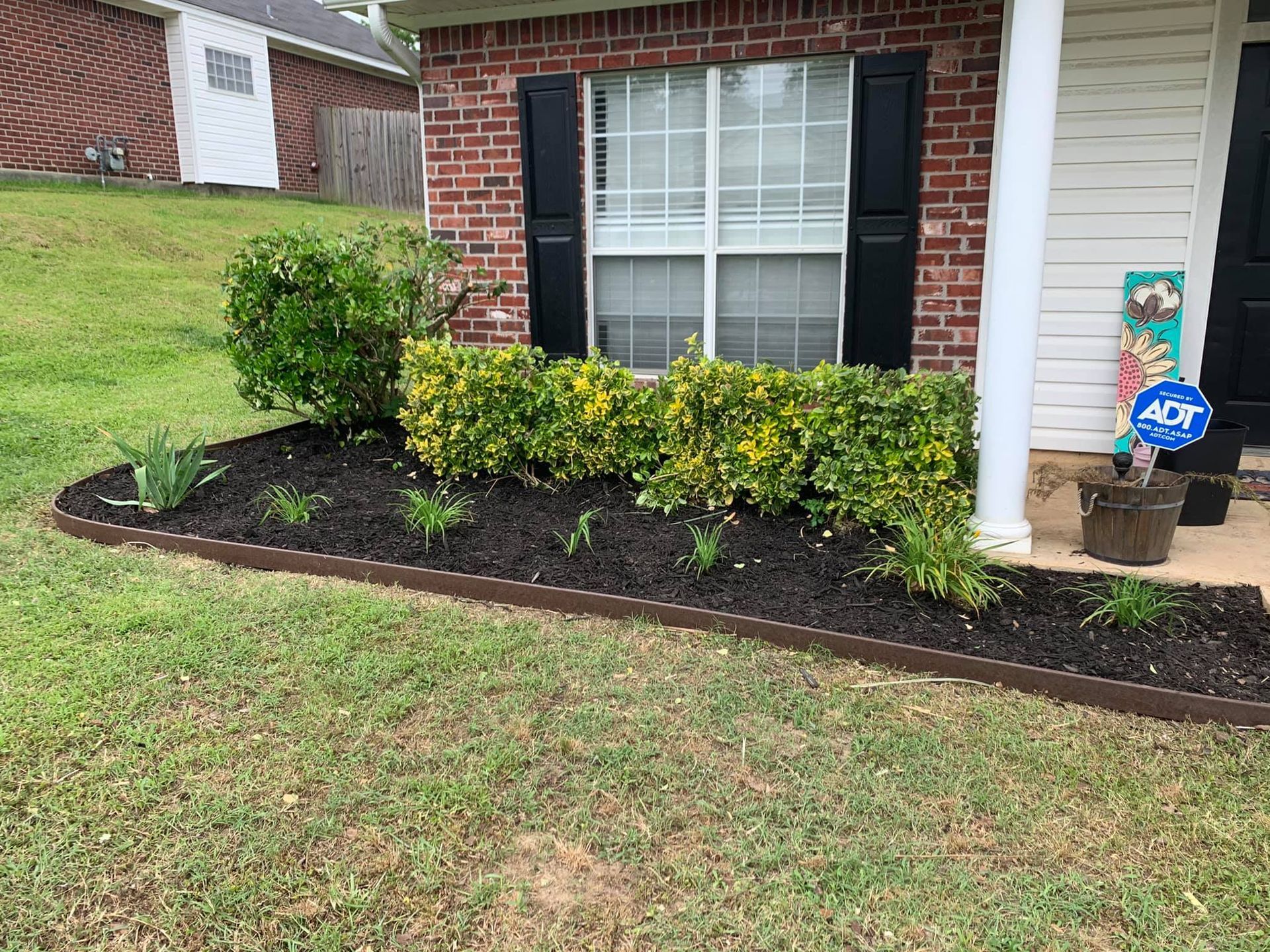 A brick house with black shutters and a garden in front of it.