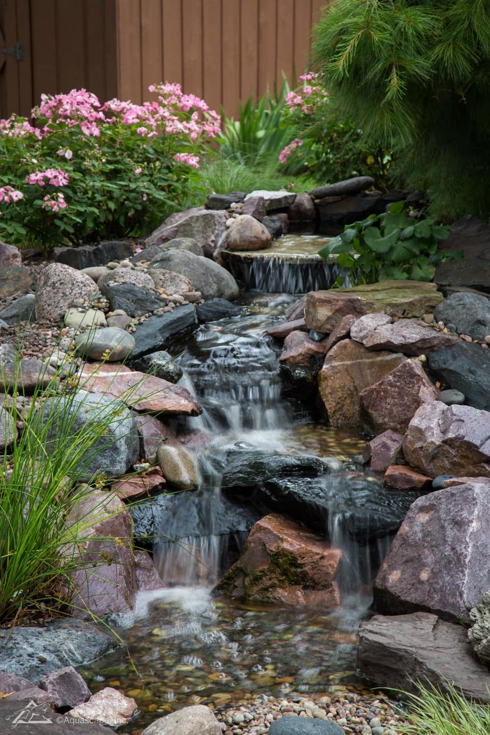 A small waterfall surrounded by rocks and flowers in a garden.