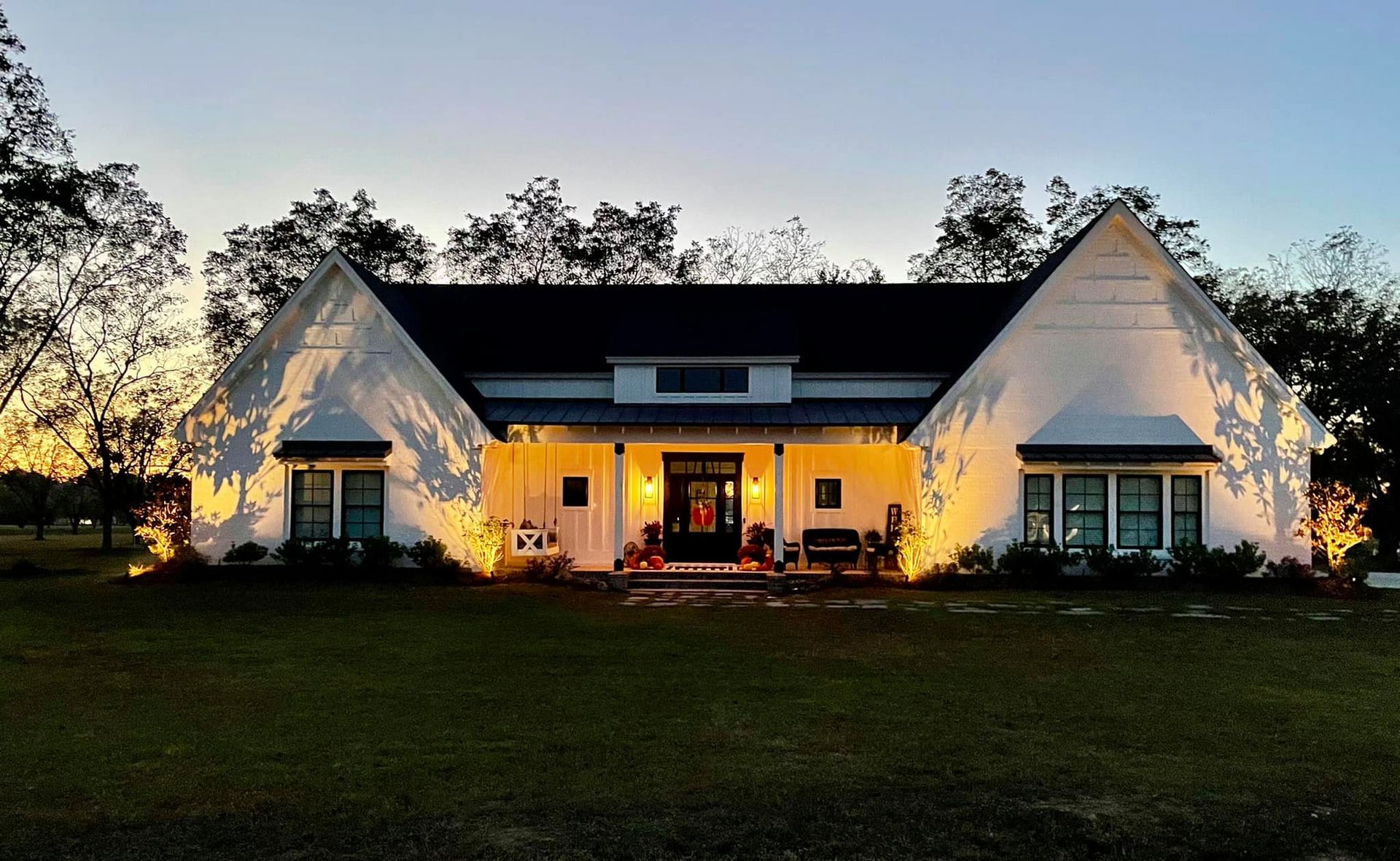 A large white house with a black roof is lit up at night.