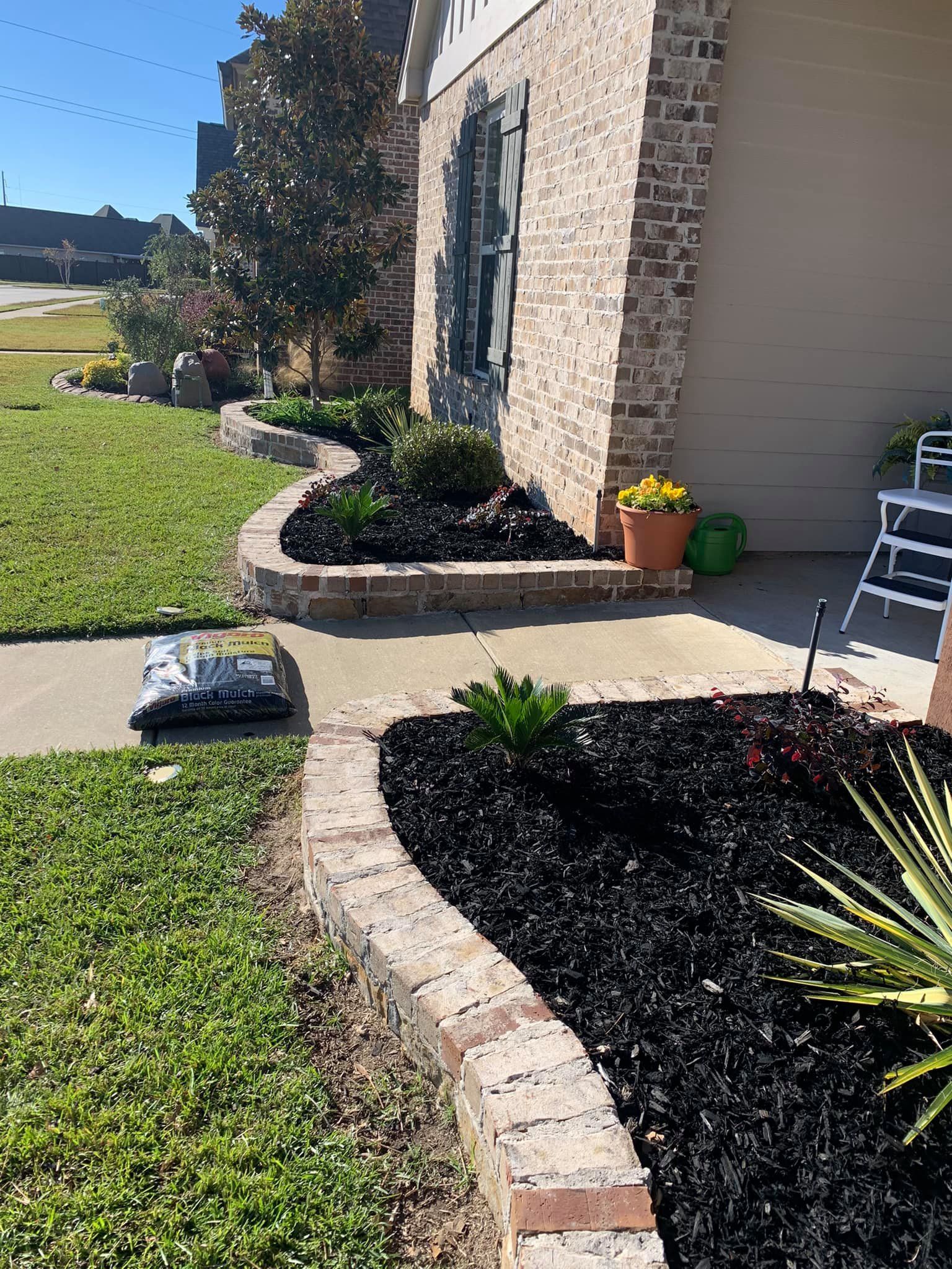 A bag of mulch is sitting on the sidewalk in front of a house.