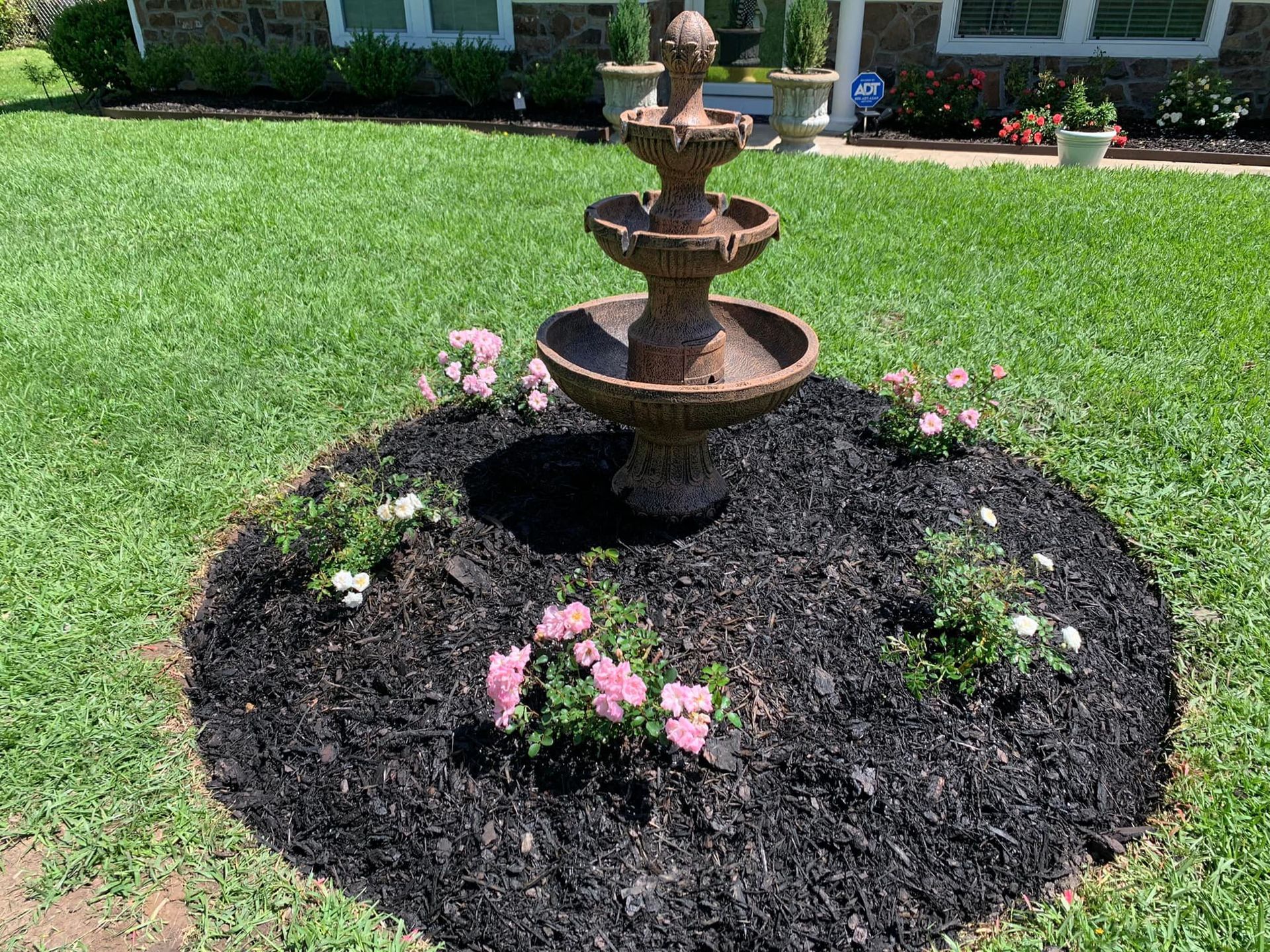 A fountain is sitting in the middle of a garden surrounded by flowers.