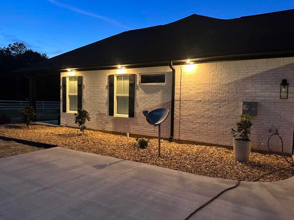 A white brick house with a black roof is lit up at night.