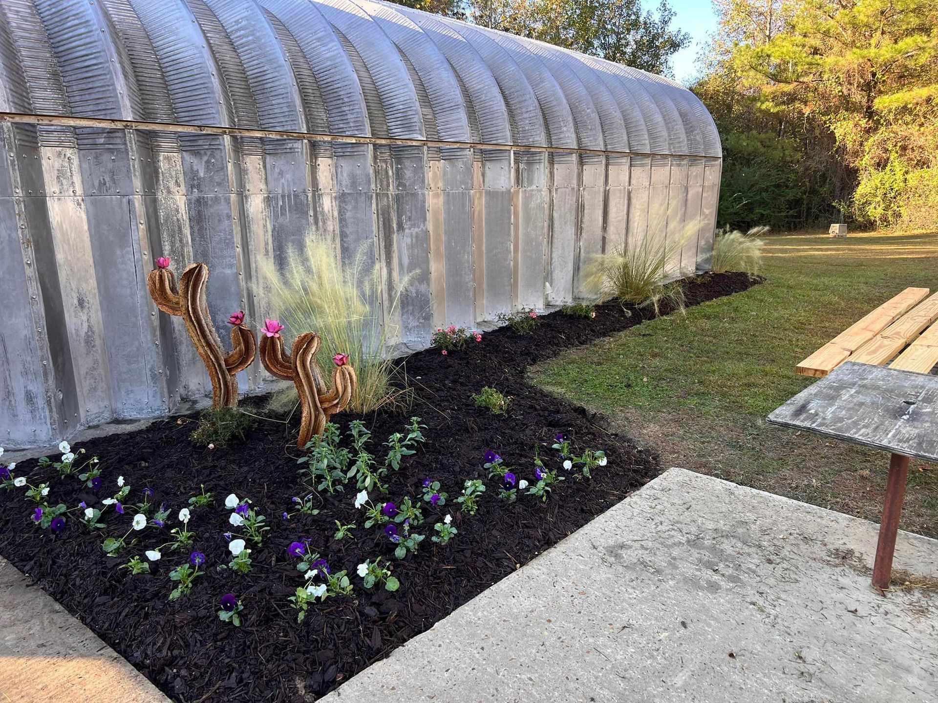 A greenhouse with flowers in front of it and a picnic table.