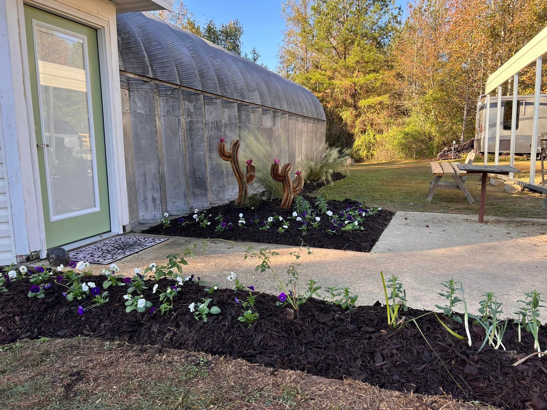 A house with a greenhouse in the background and a garden in front of it.