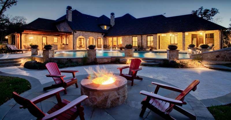 A fire pit with chairs around it in front of a large house.