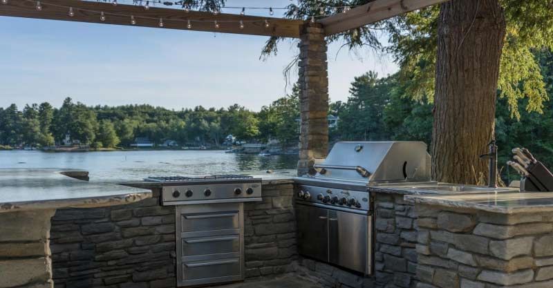 An outdoor kitchen with a grill and a view of a lake.
