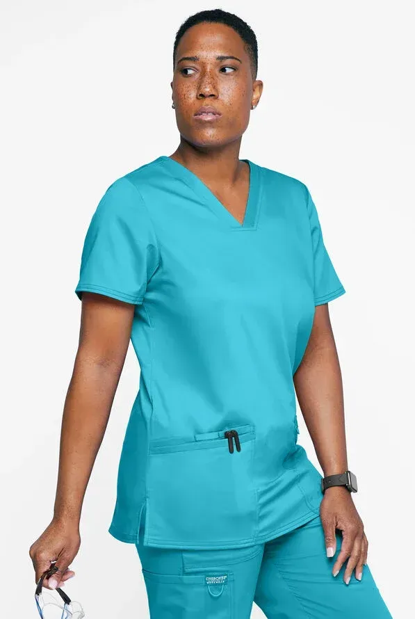 Woman in teal scrubs looks away, holding glasses.