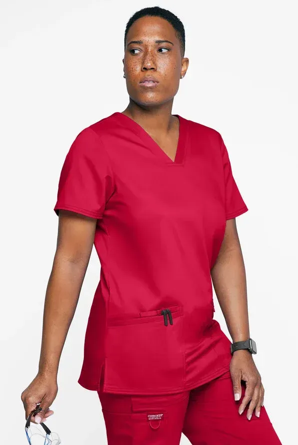 Person wearing red scrubs, holding medical equipment, looking to the side.