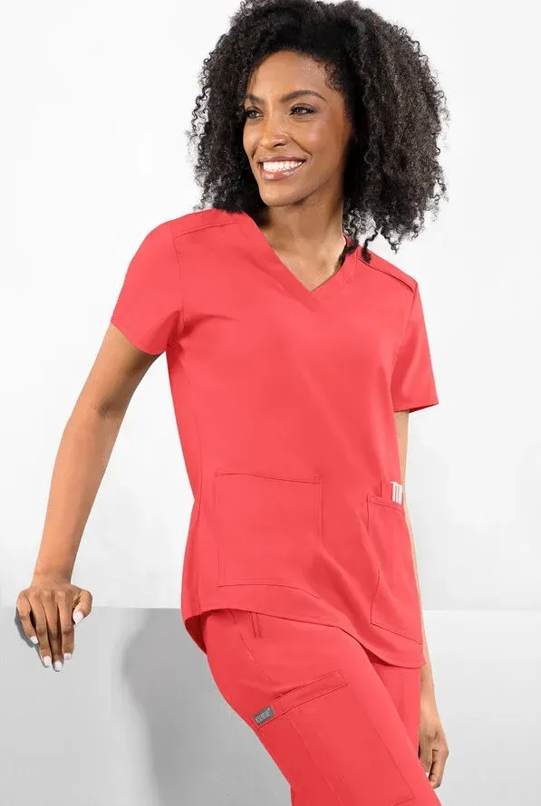 Woman in red scrubs smiling, leaning against a white surface.