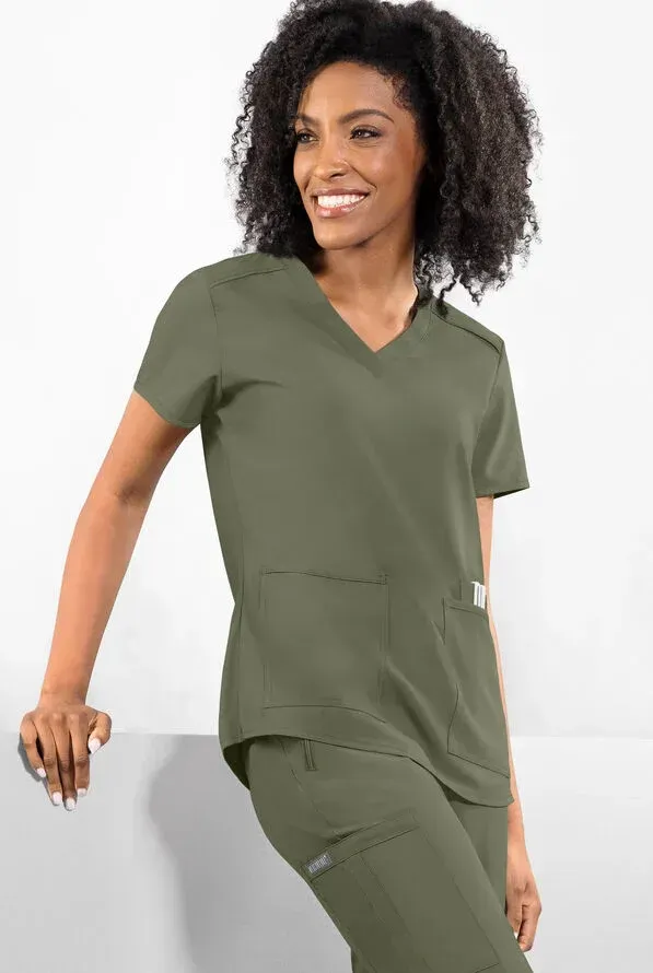 Woman in olive-green scrubs, leaning on a white surface, smiling.