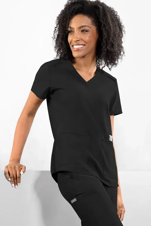 Woman in black scrubs smiling, leaning against a white surface.
