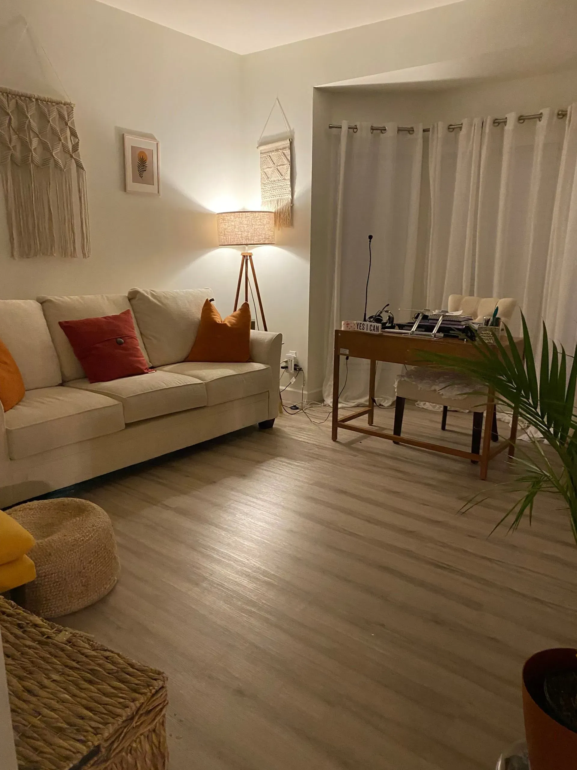 A living room with a couch , desk , chair and lamp.