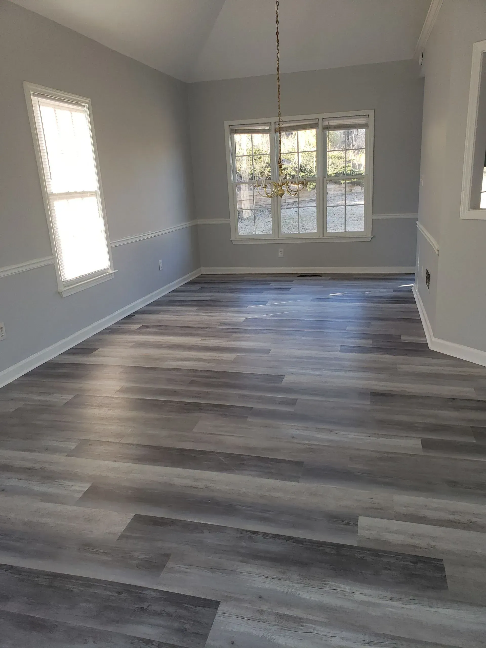 An empty living room with hardwood floors and a chandelier.
