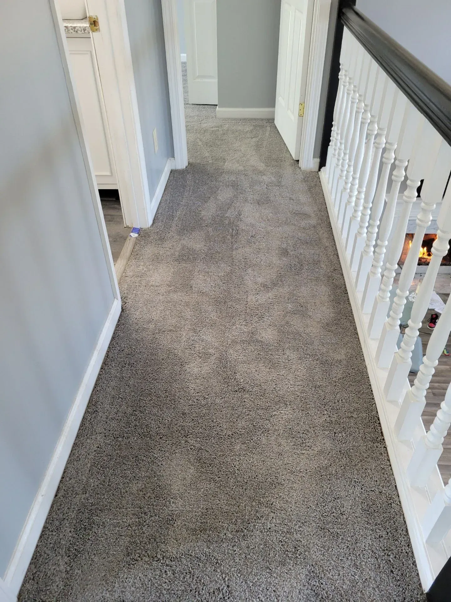 A hallway with a carpeted floor and stairs in a house.