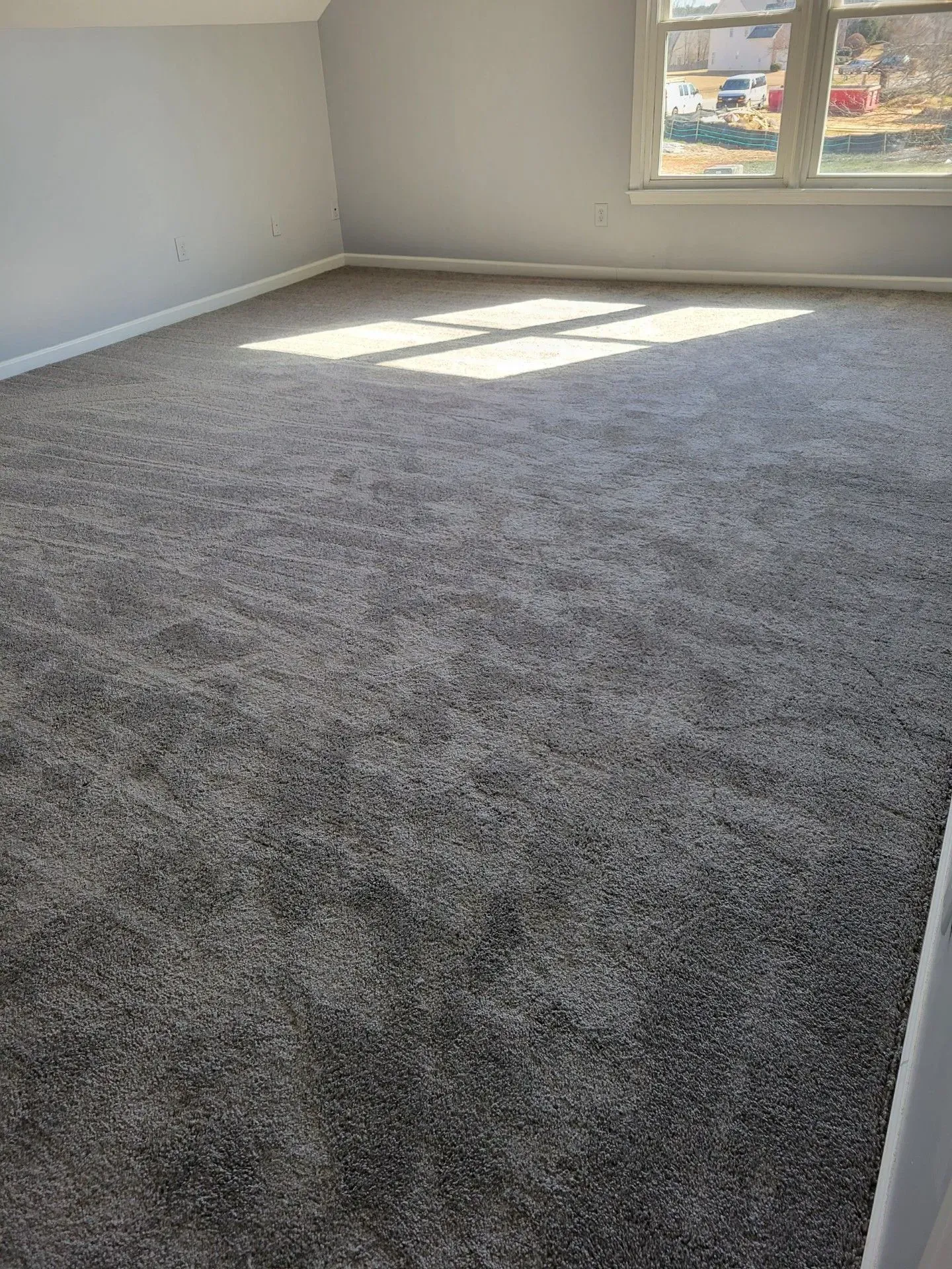 An empty room with a large carpeted floor and a window.