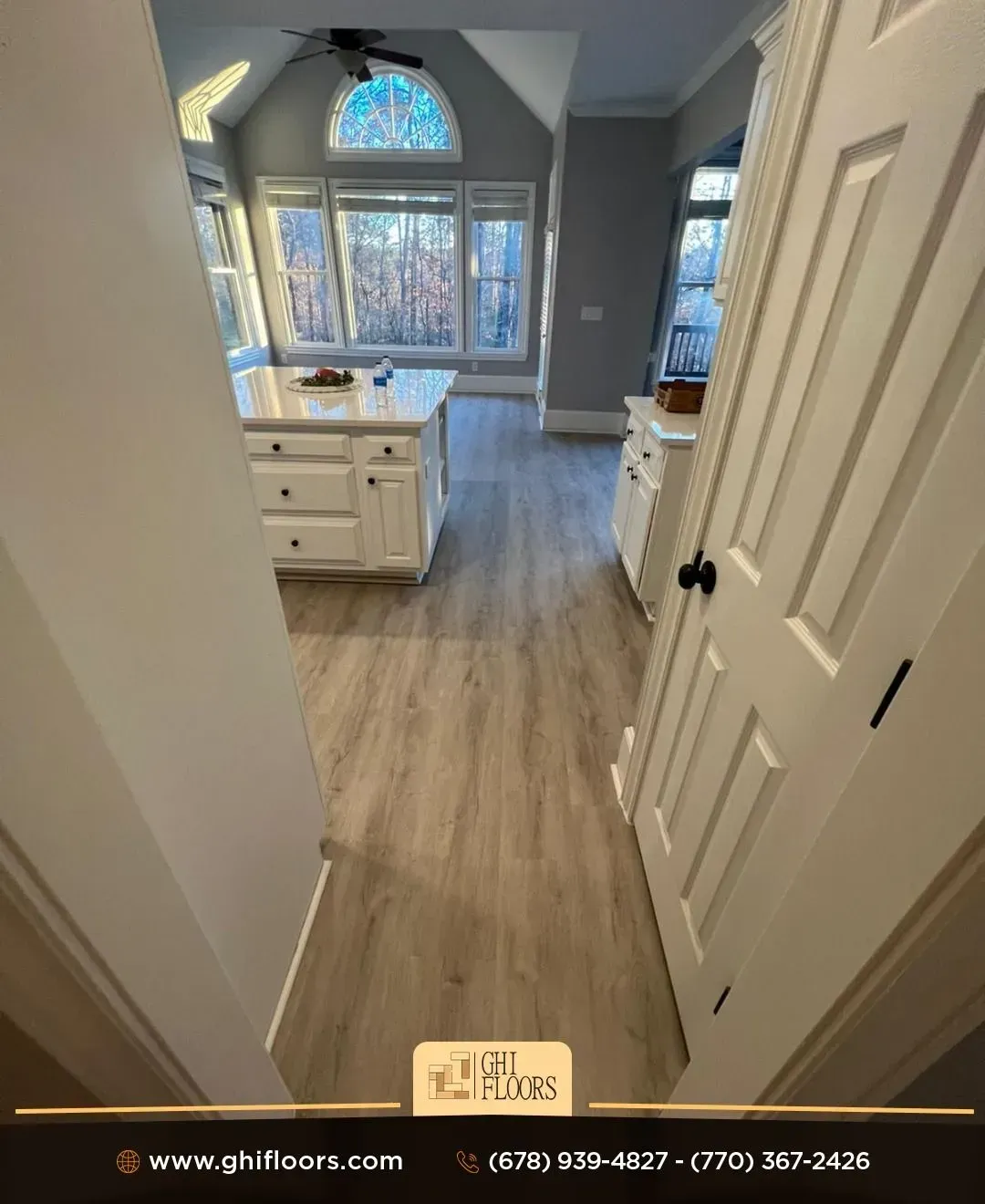 A hallway leading to a kitchen with hardwood floors and white cabinets.