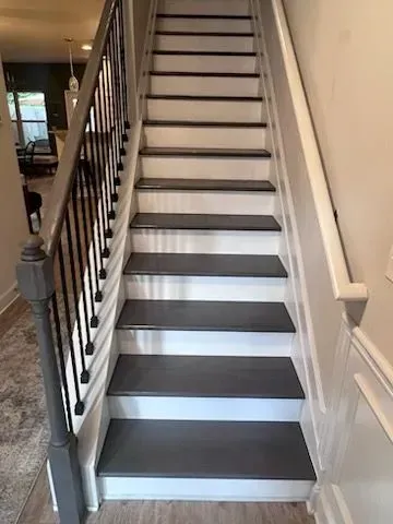 A set of stairs with gray steps and a black railing in a house.