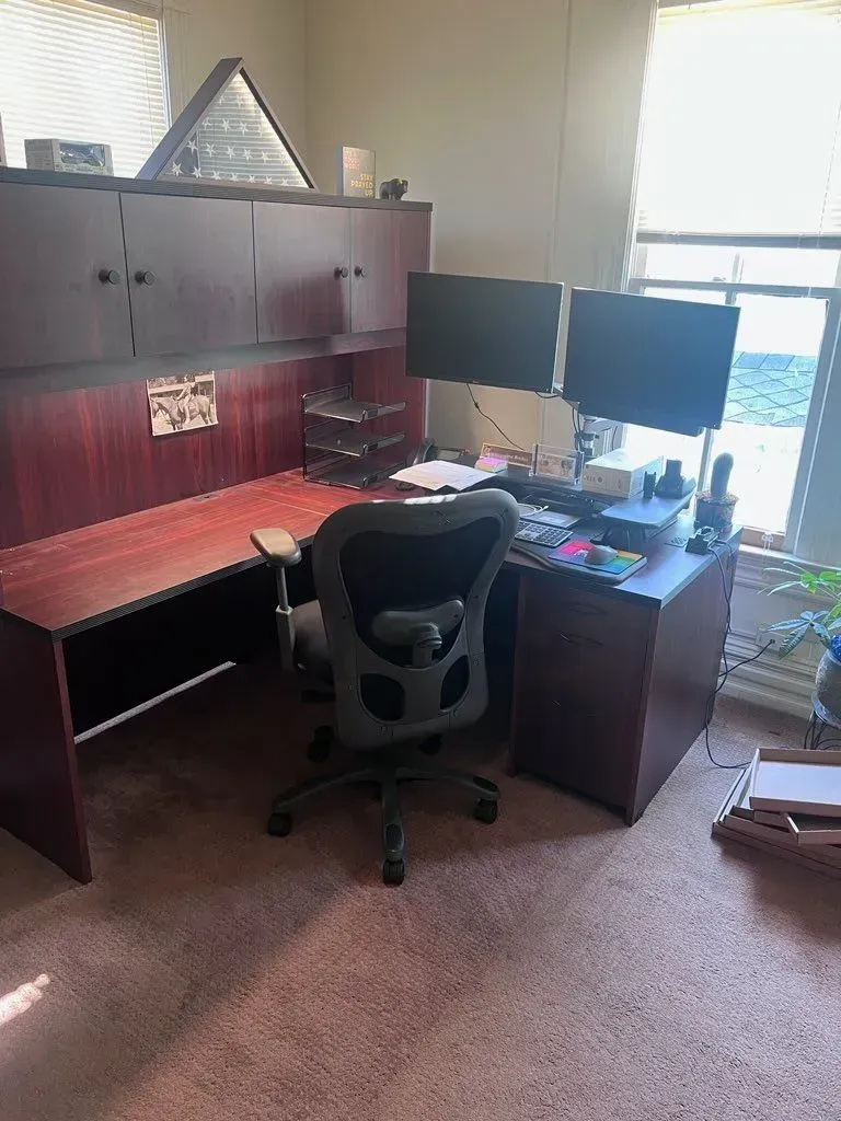 A desk with two monitors and a chair in a room.