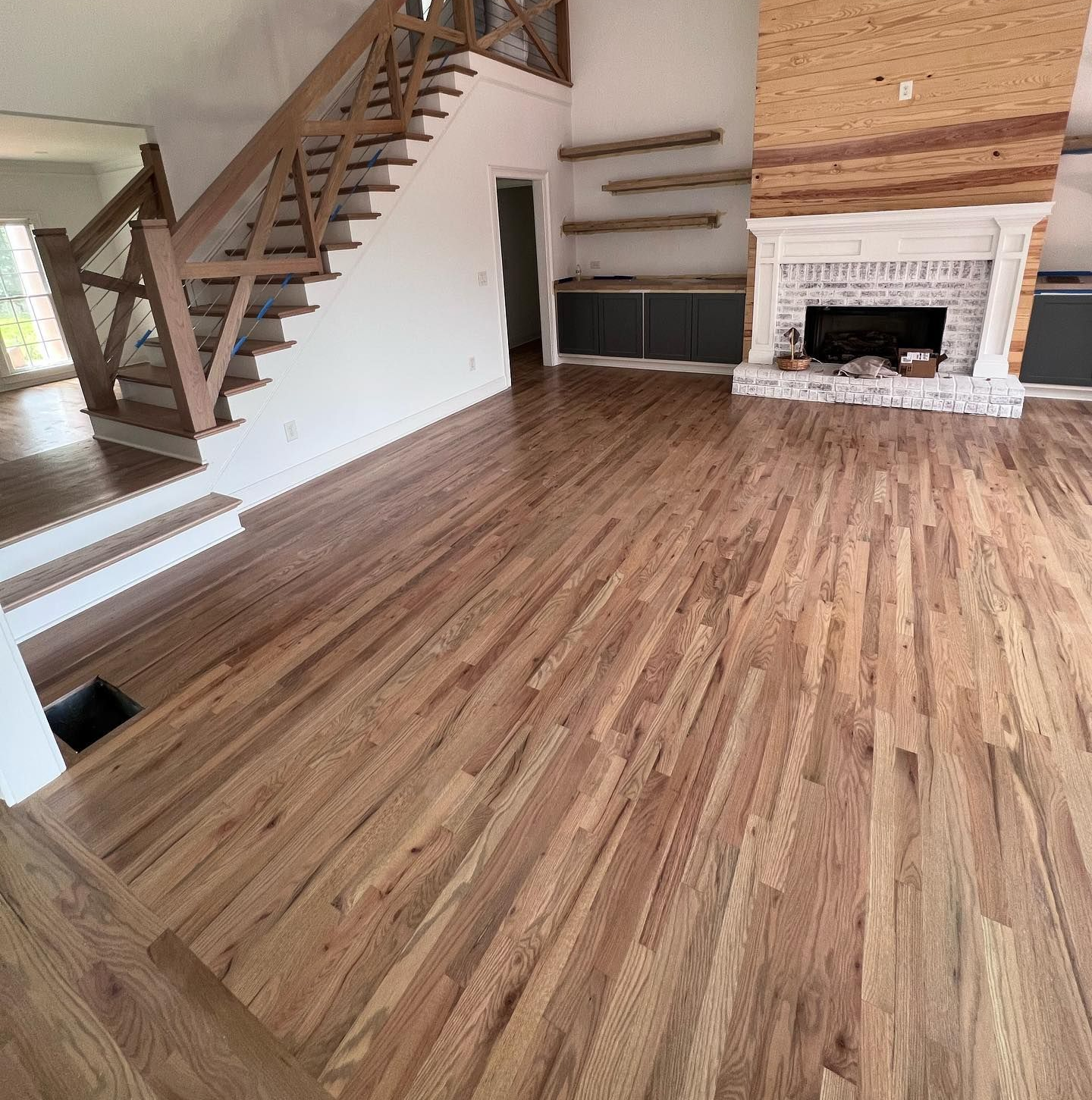 Empty living room with wood floors, staircase, built-in shelves, and a brick fireplace.