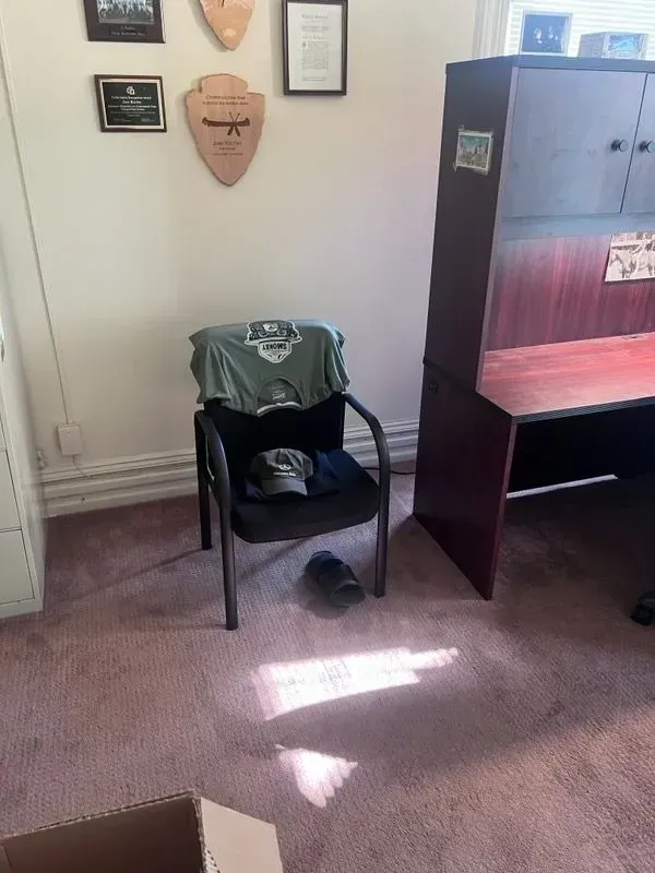 A chair with a shirt on it is in a room next to a desk.