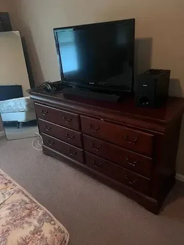 A bedroom with a dresser , television , speakers and a mattress.