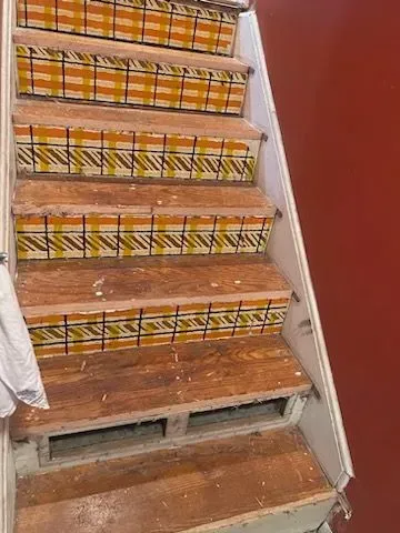 A wooden staircase with tiles on the steps and a red wall.