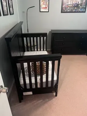 A black crib is sitting in a room next to a dresser.