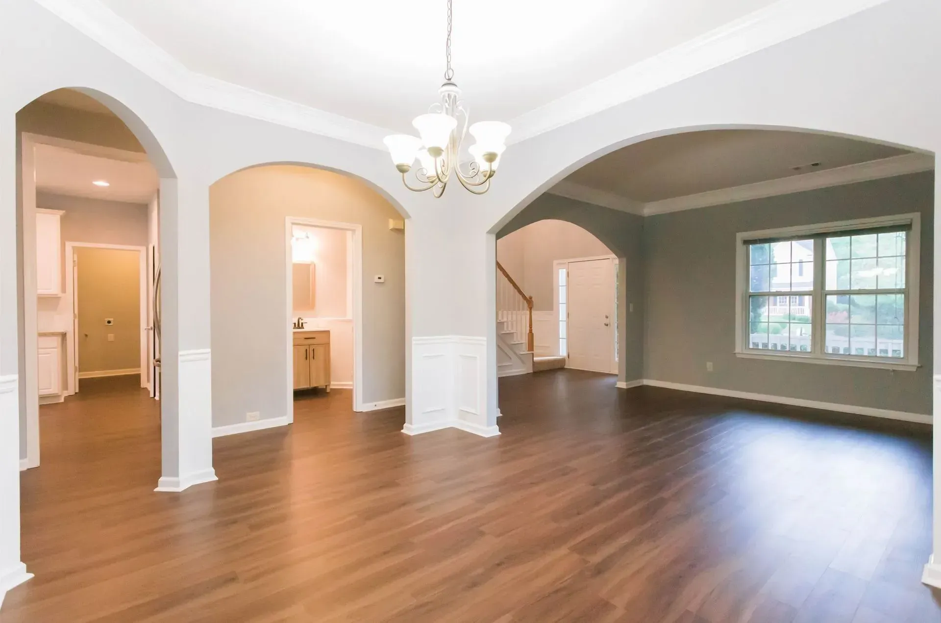 An empty living room with hardwood floors and a chandelier.