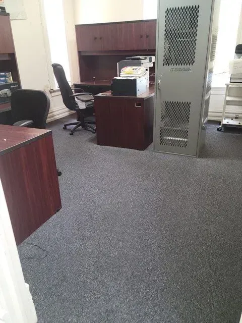 A gray carpeted office with a desk and chairs