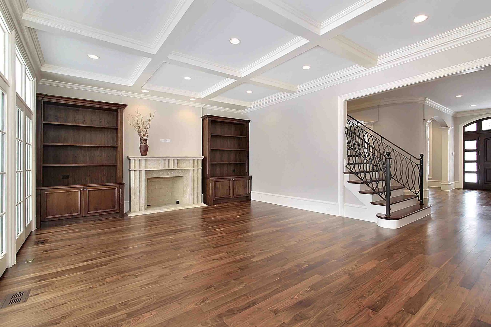 Empty, elegant living room with built-in bookshelves, fireplace, hardwood floors, and ornate ceiling.