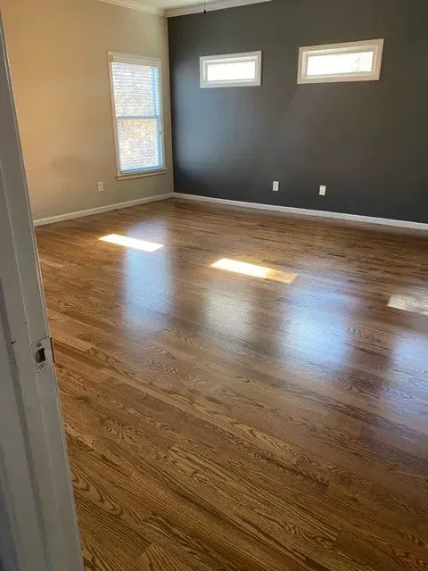 A large empty room with hardwood floors and a gray wall.