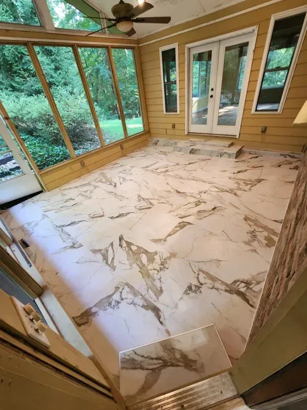 A screened in porch with a marble floor and ceiling fan.