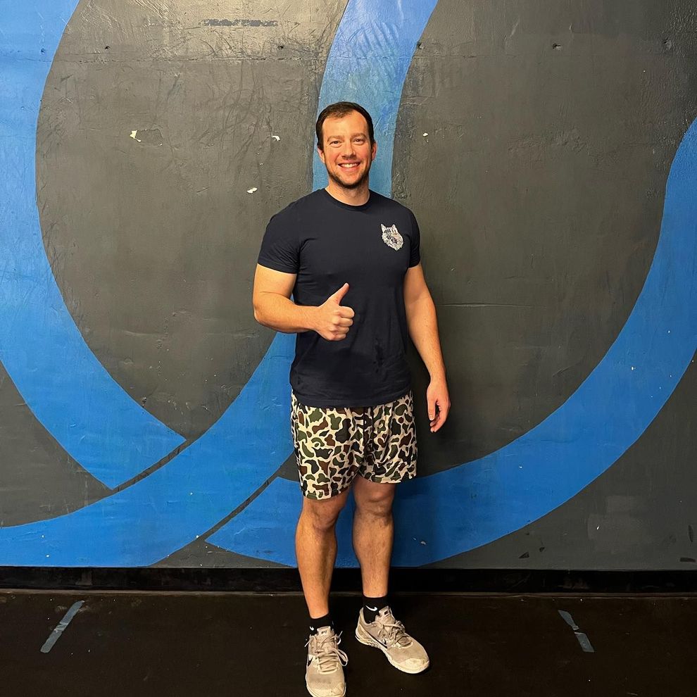 A man in a black shirt and shorts is giving a thumbs up