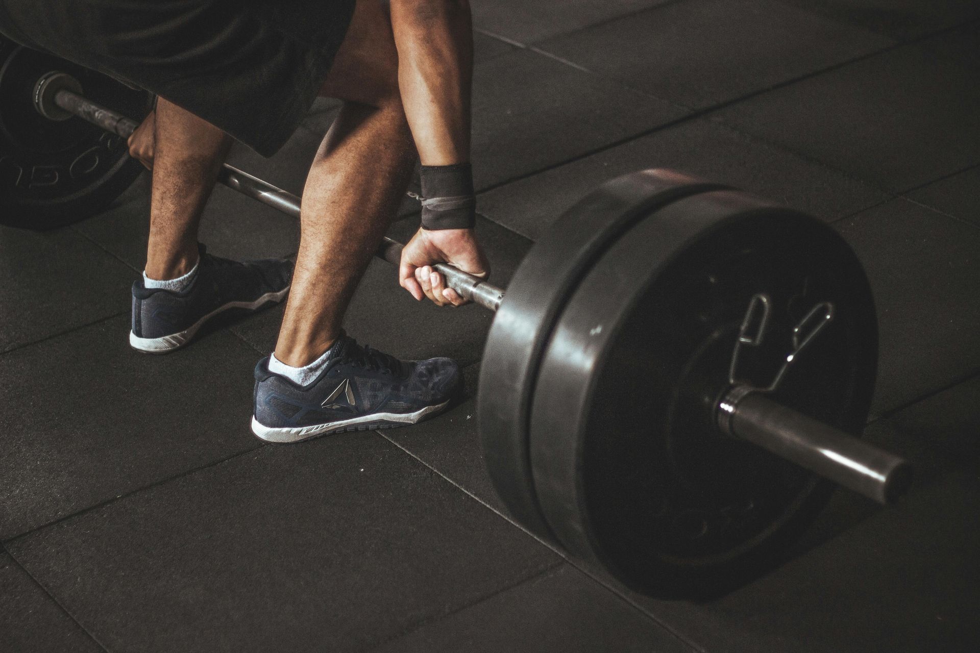Man lifting a heavily weighted barbell in a gym. Dark setting, black weight plates, wrist wraps, focused expression.