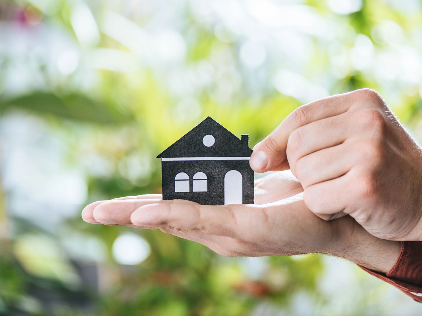 Persona che tiene nel palmo della mano una piccola casa di carta nera.