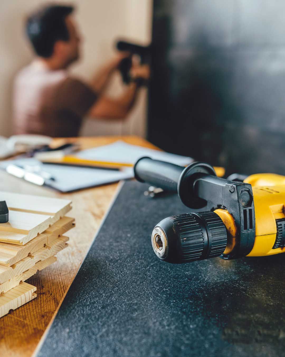 Trapano giallo su un tavolo con un uomo sullo sfondo che usa un trapano.