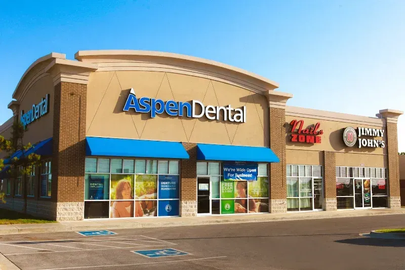 A dental office with a blue awning and a sign that says aspen dental