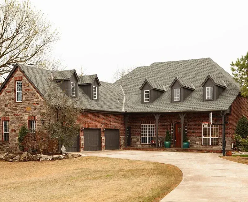 A large brick house with a gray roof and two garages