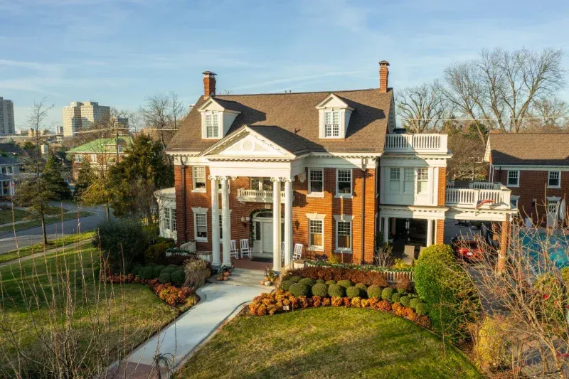An aerial view of a large brick house with a large lawn in front of it.